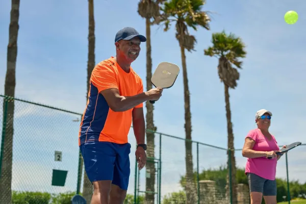 A smiling man having a casual pickleball rally on a Bermuda court