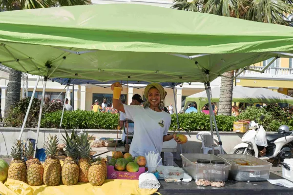 A woman holds up a tropical fruit smoothie at an outdoor stand