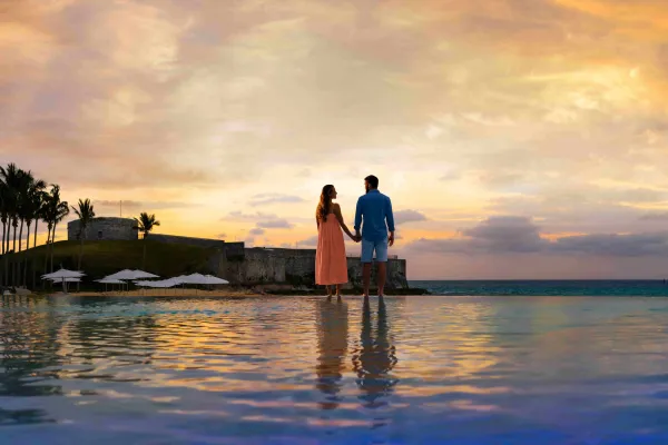 A couple stands holding hands next to a pool at dusk