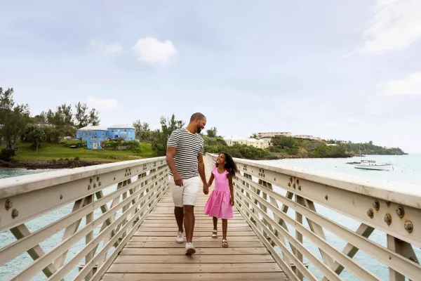 A father and daughter are walking along a bridge smiling.