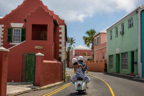 A couple is riding a scooter by colourful buildings.