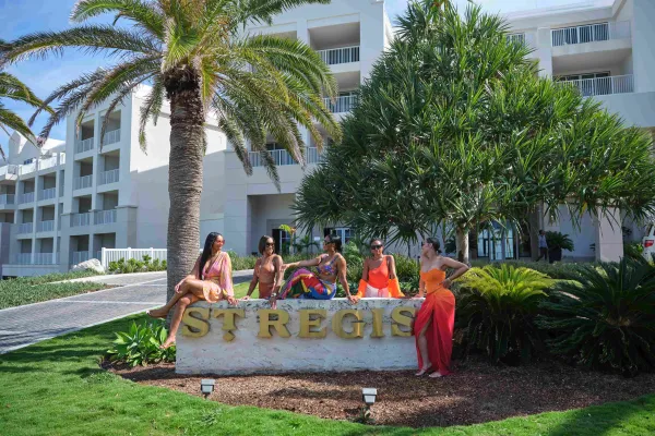 A group of friends are sitting on the St. Regis Bermuda hotel sign.