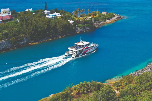 A ferry is riding out of St. George's with calm blue waters.