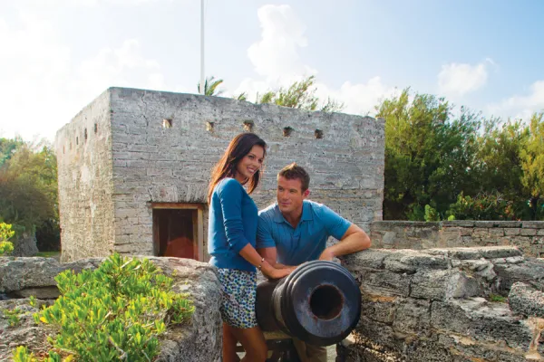 A couple is standing by a canon near a fort. 