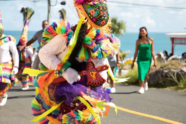 A close up of a gombey dancer with people dancing and walking behind.