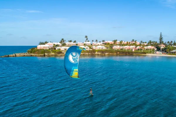 A person is kiteboarding on calm blue waters with a pink hotel in the background.