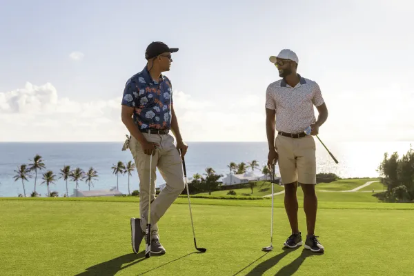 Two men are standing on a golf course talking. 
