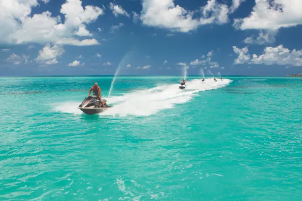 A group of guys are travelling on jetskis.