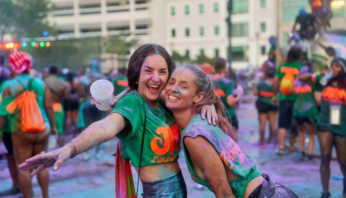 Two laughing girls covered in coloured powder hugging after participating in a colour run