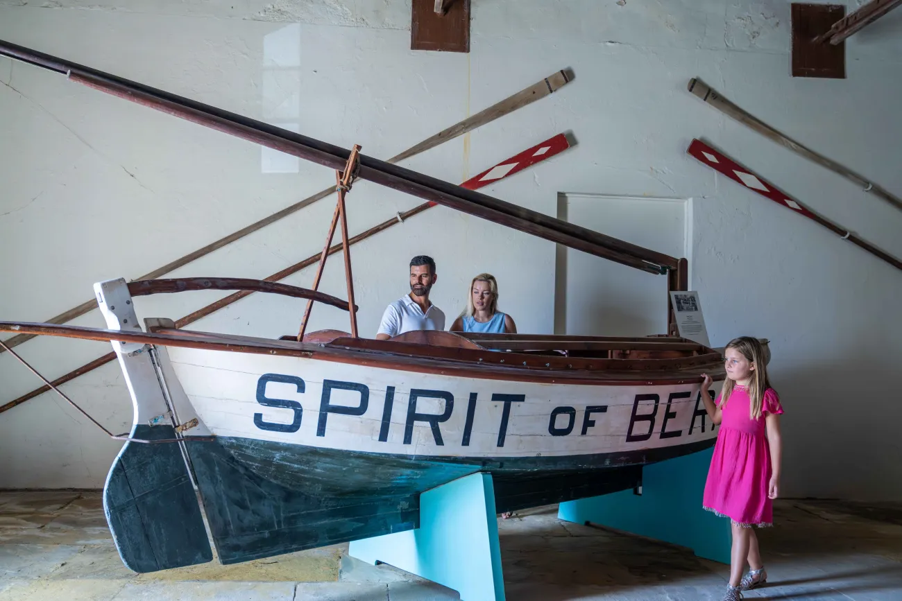 A family are standing by an old historic boat called the Spirit of Bermuda
