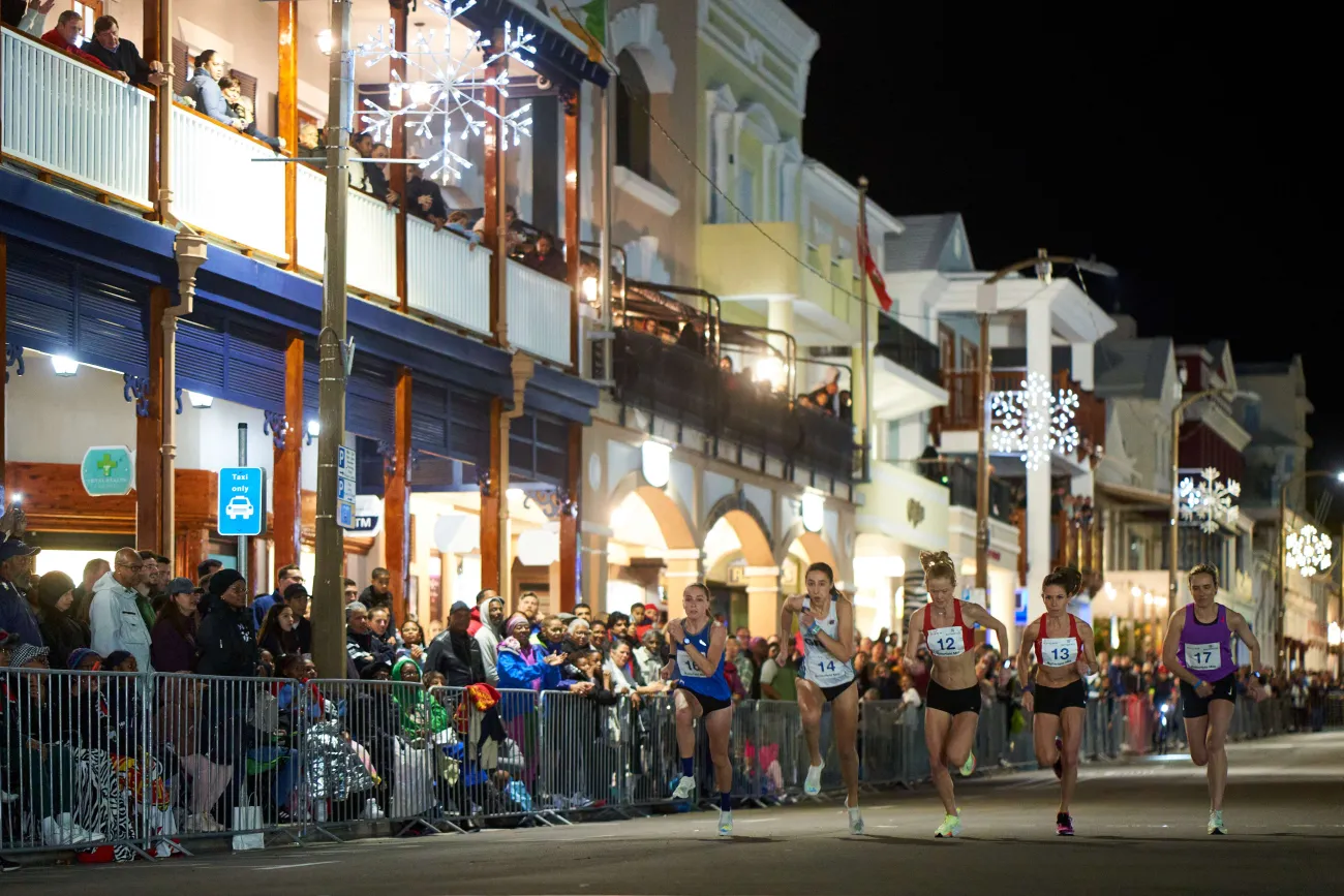 A group of women are running on Front Street with a crowd looking on.