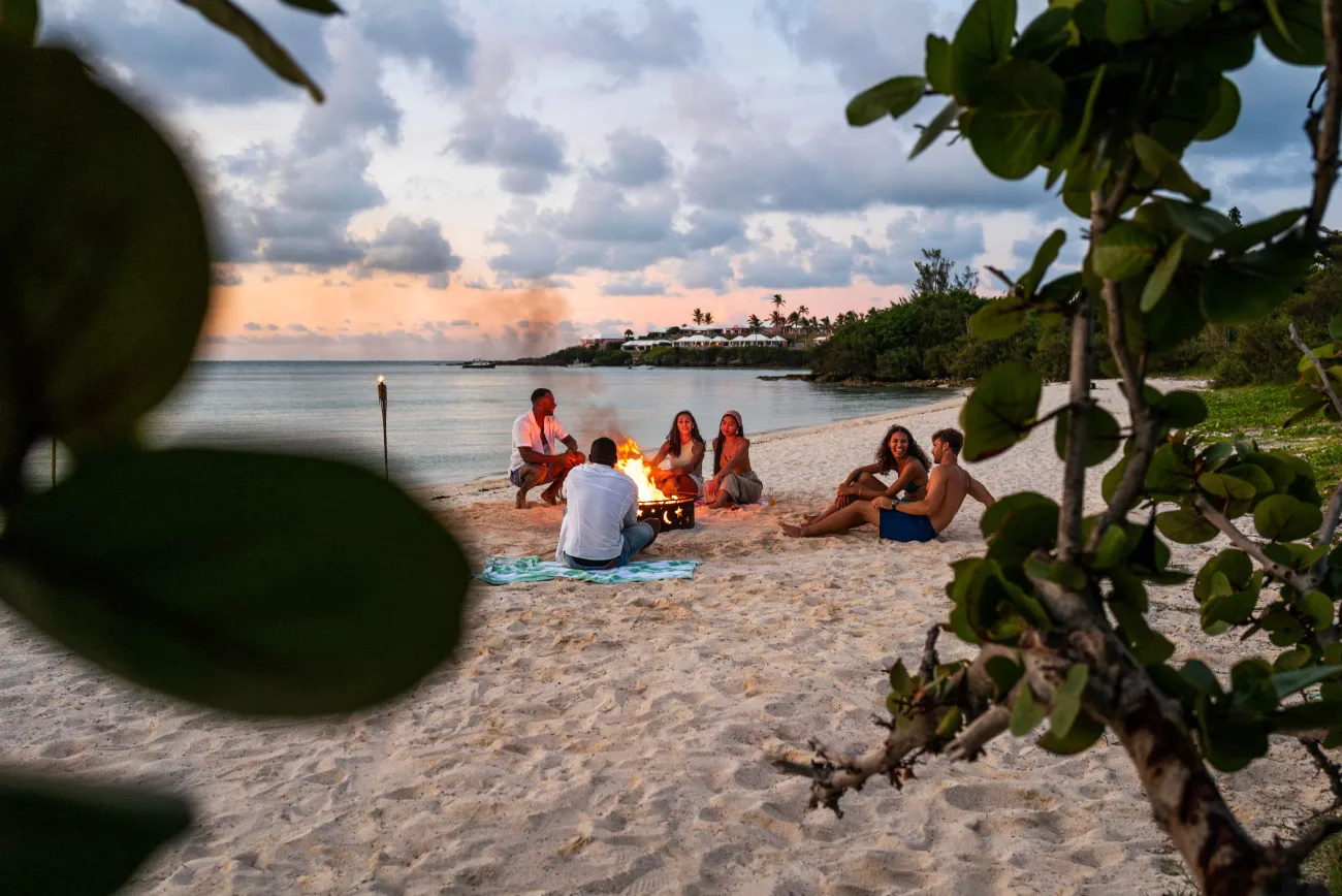A group of friends are sitting on the beach around a bonfrie.