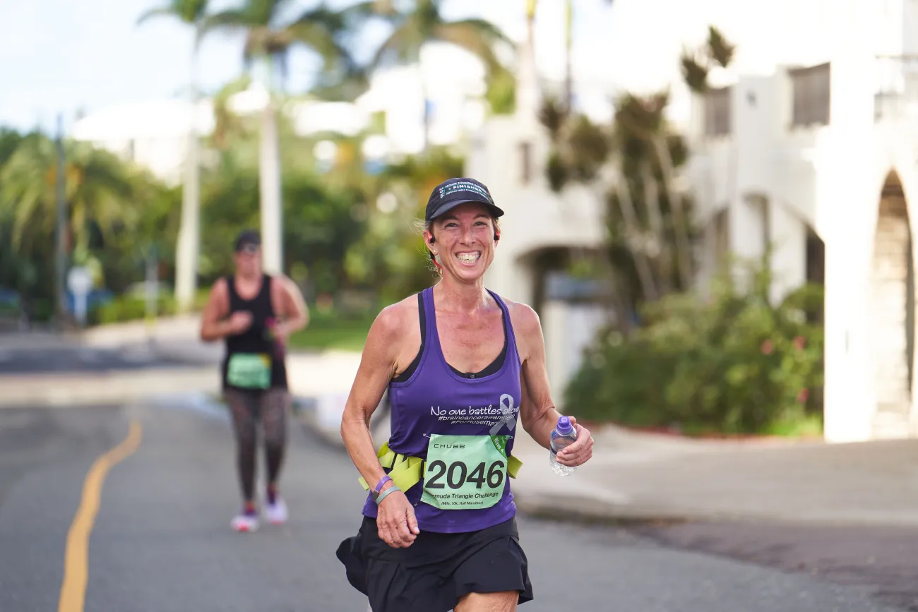 A woman is smiling at the camera while running the PWC Half Marathon.