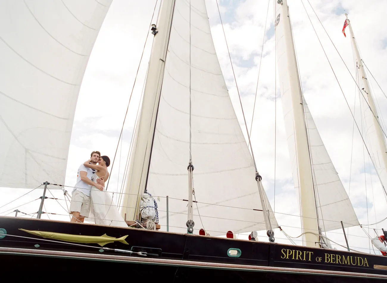 A couple is hugging on an old sail boat.