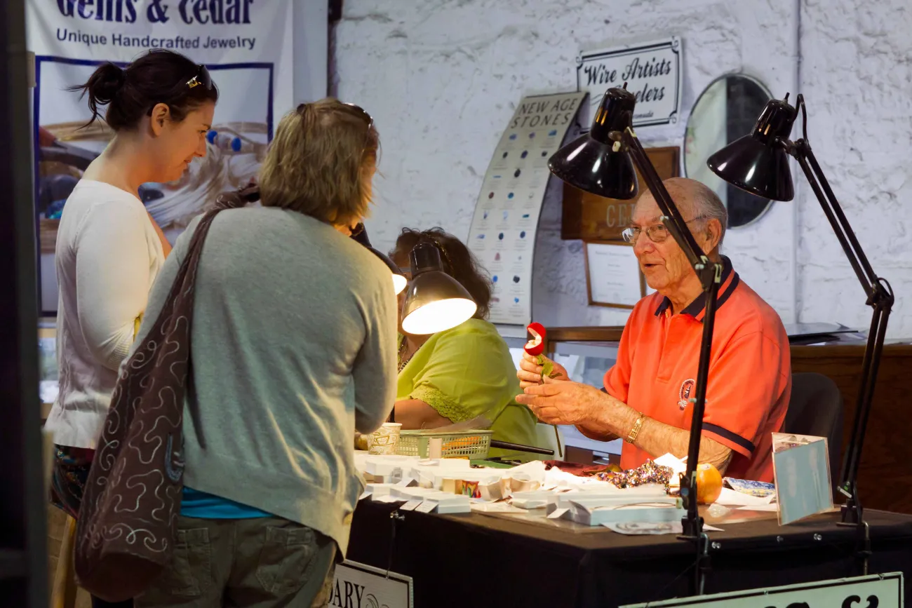 A man is showing his crafts to two women at the Bermuda Craft Market.