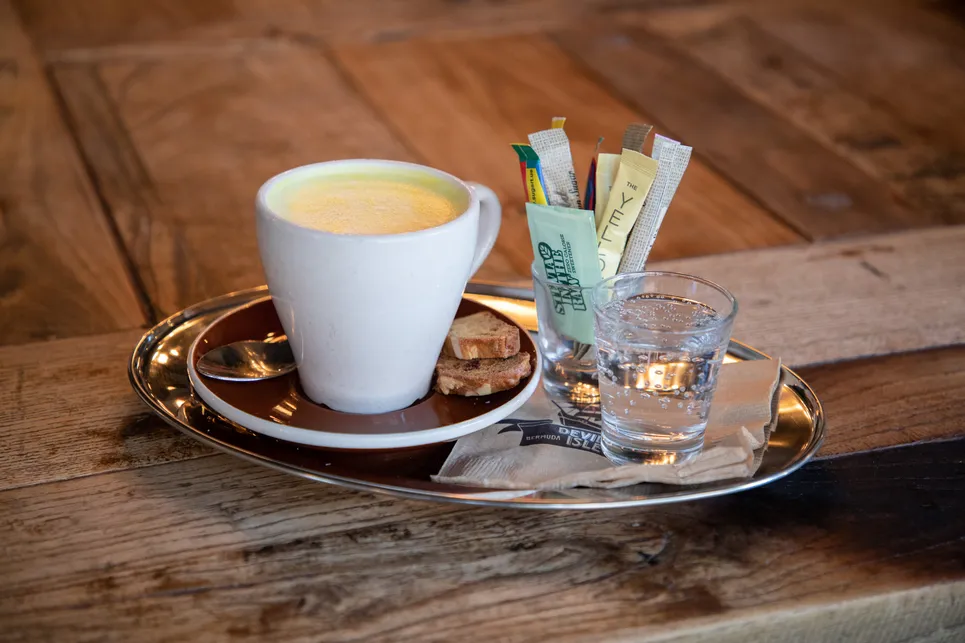 A close up of a tray with a coffee cup, sugar, and sparkling water. 