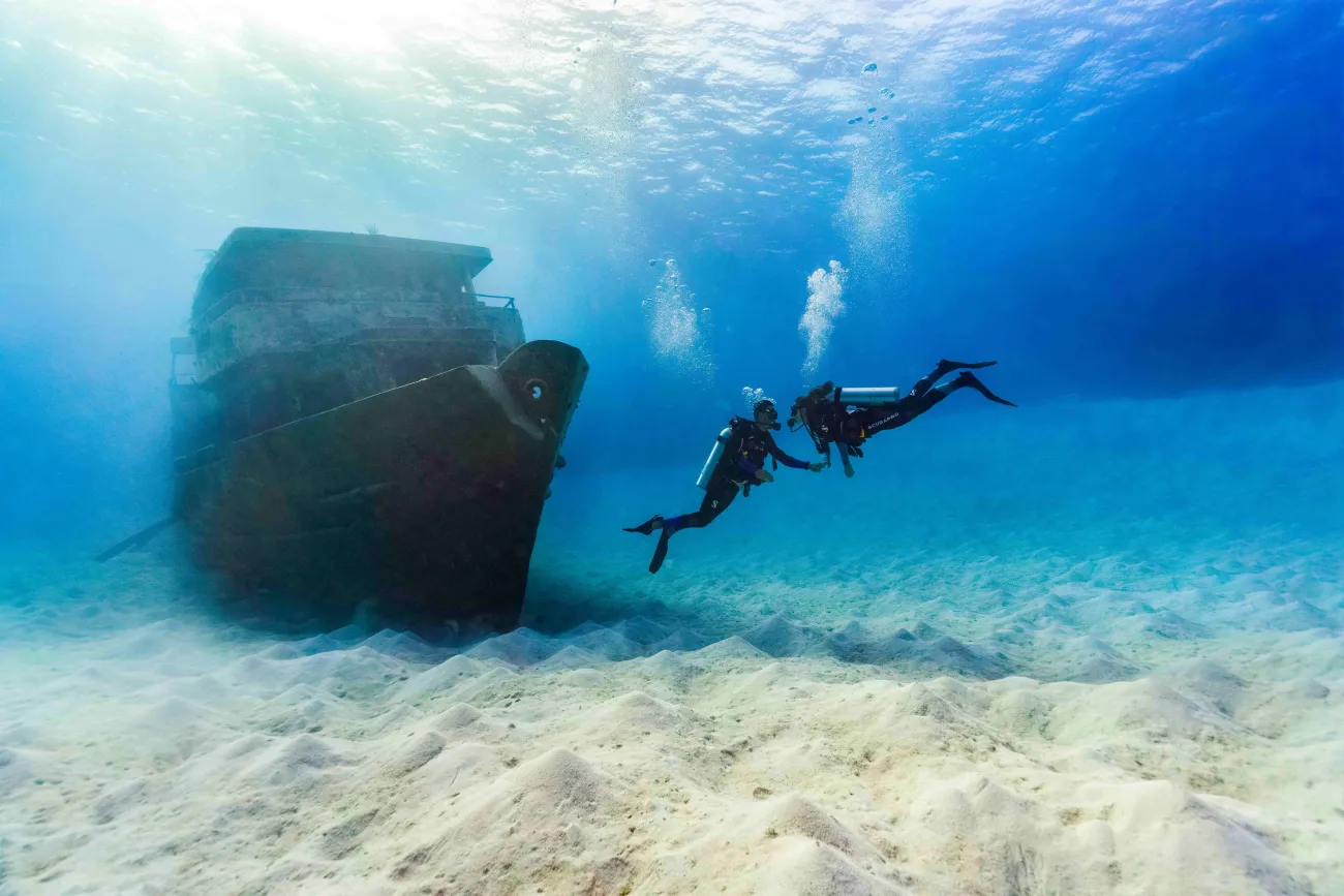 A couple is holding hands under water by a shipwreck