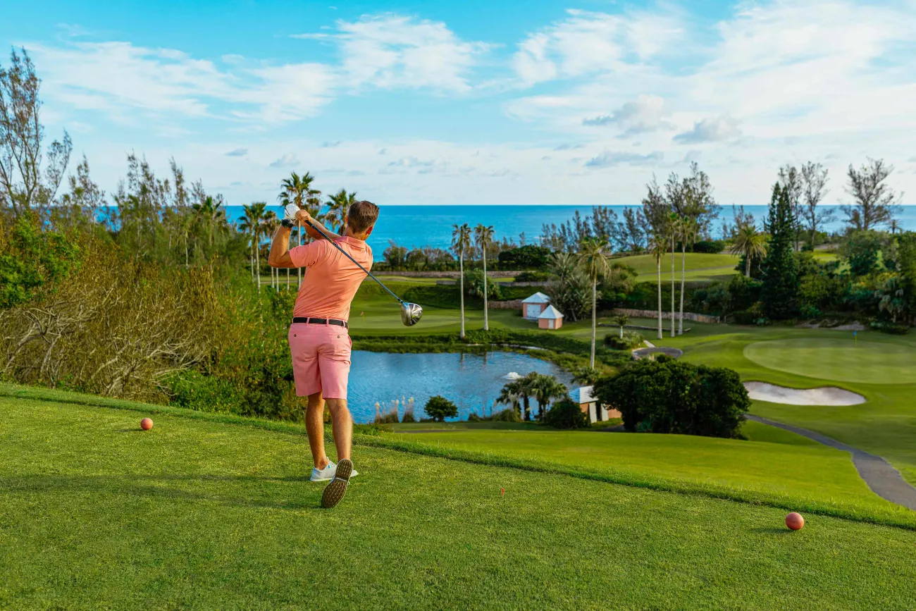 A man is teeing off on a scenic course with the ocean in the background.