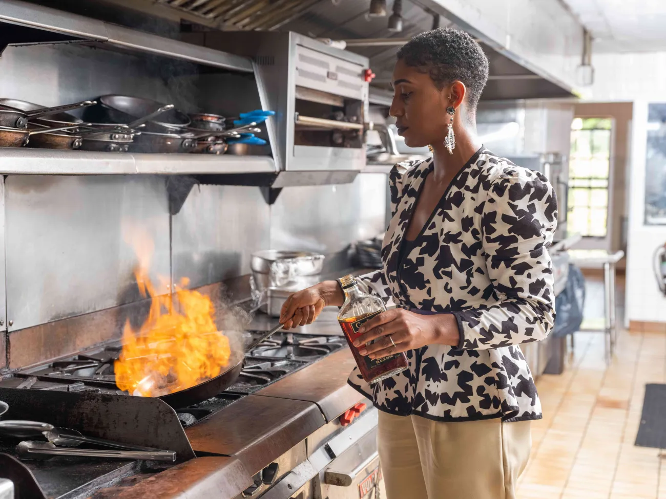 A woman is in a kitchen cooking in a pan with flames showing.