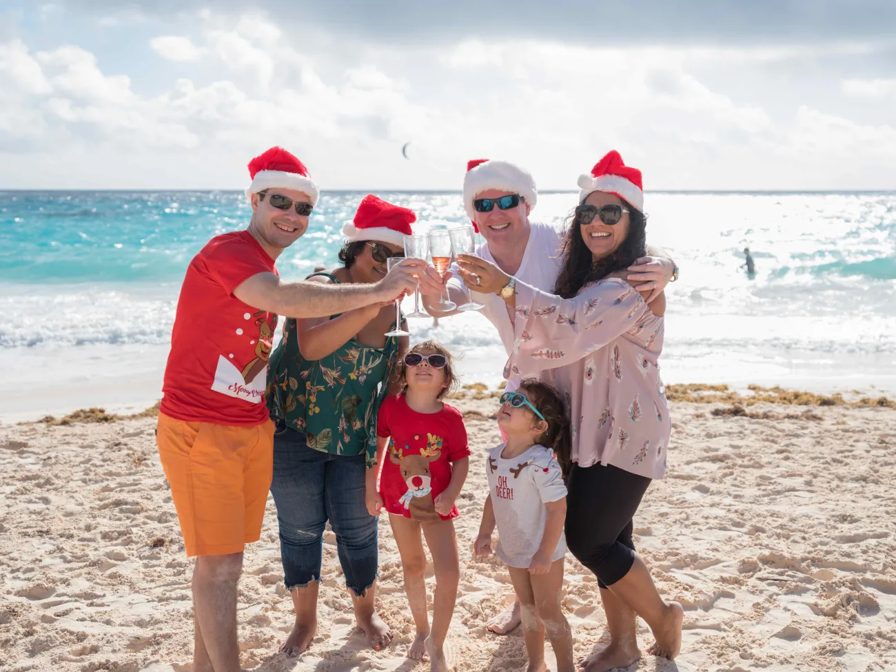 A family is cheering while on the beach in Christmas gear.
