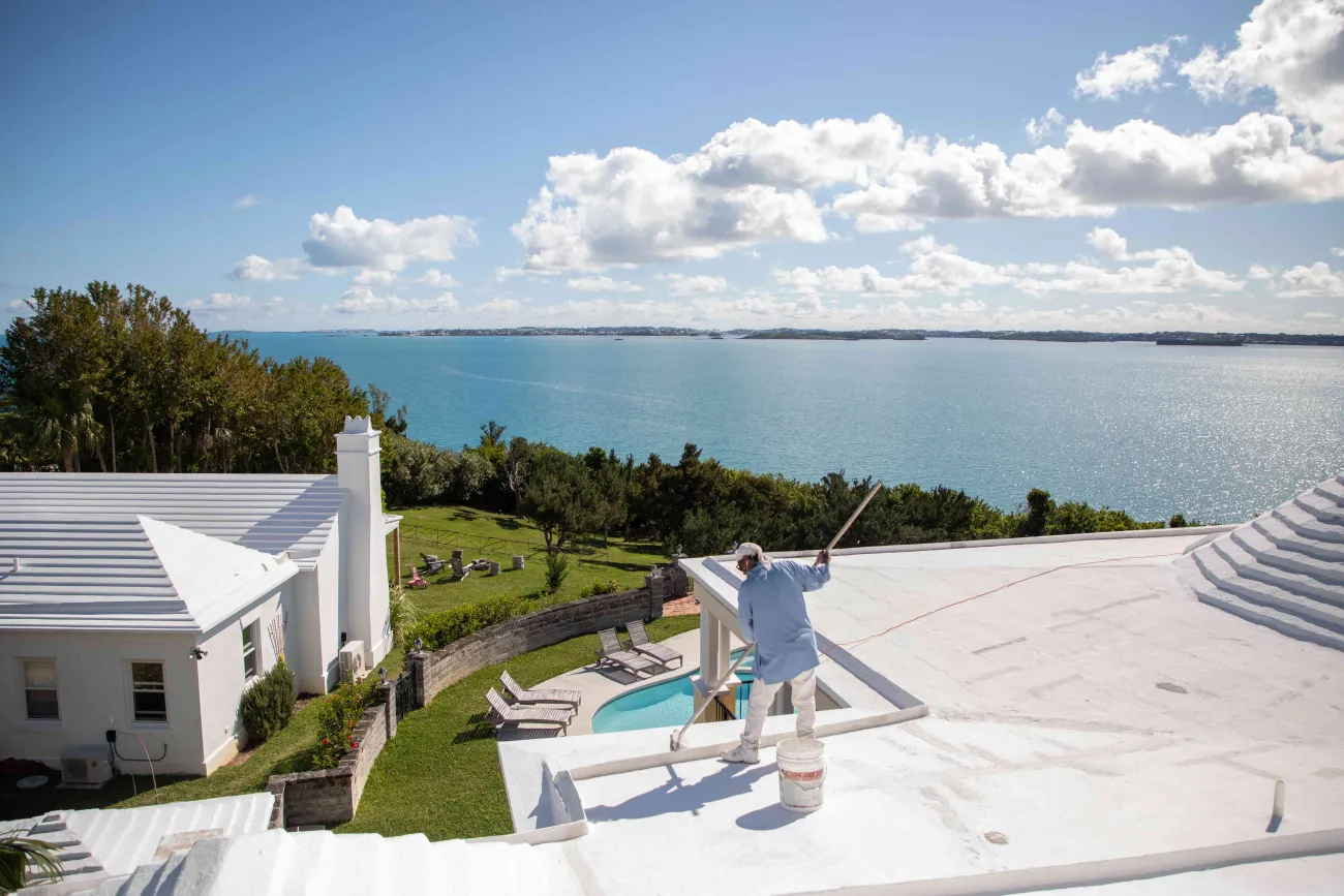 A man is painting a Bermuda roof with white paint.